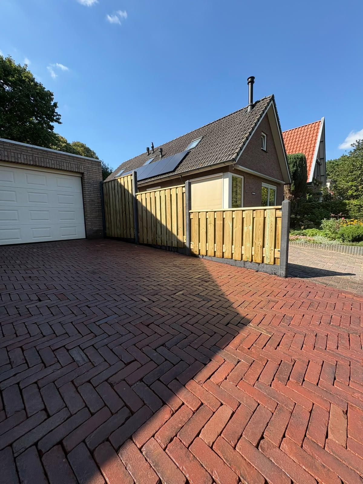 Nieuwe oprit in gebakken klinkers met houten schutting langs de garage door Franke Tuinen