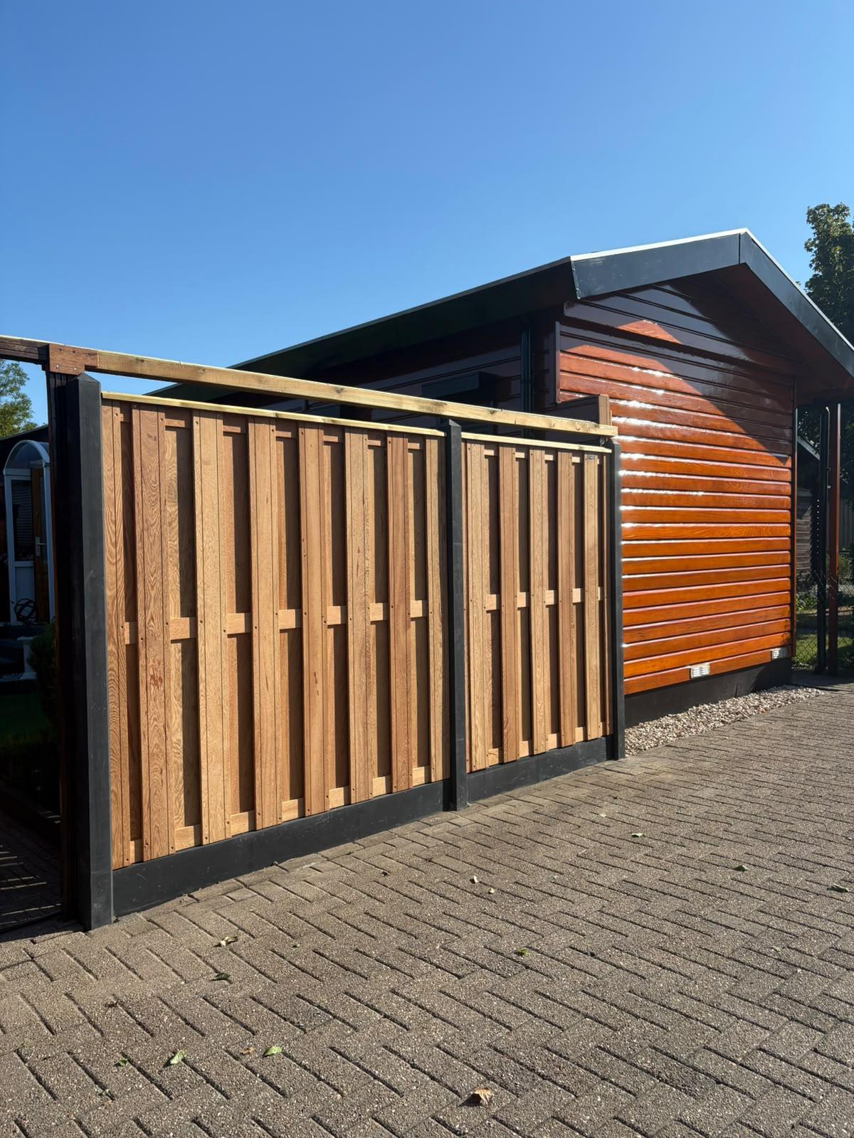 Moderne houten schutting met verticale planken en zwart stalen frame geplaatst door Franke Tuinen