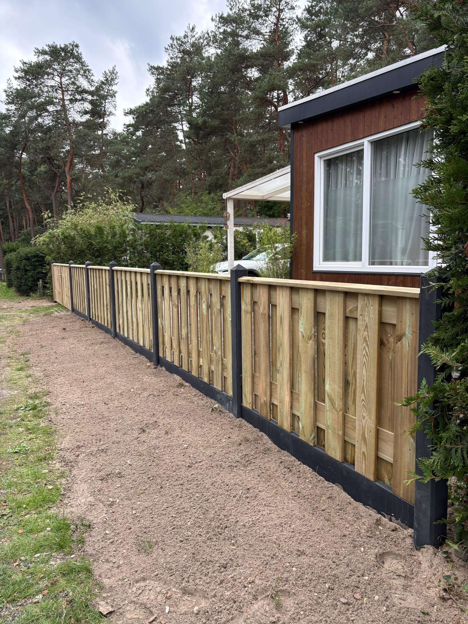 Nieuwe houten schutting met zwart stalen palen naast vakantiehuisje door Franke Tuinen