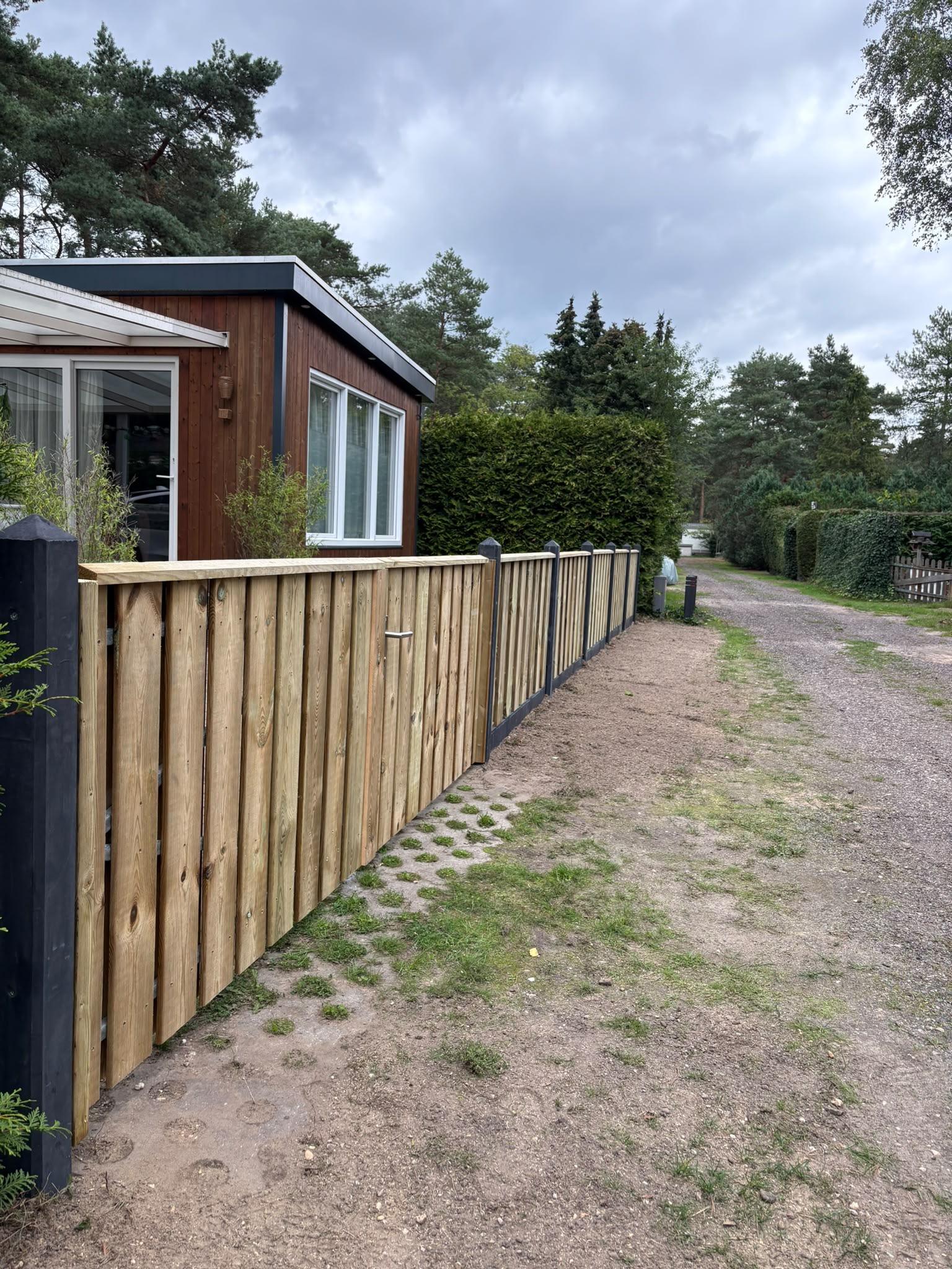Dezelfde erfafscheiding na plaatsing — hoge houten schutting met zwart stalen palen door Franke Tuinen