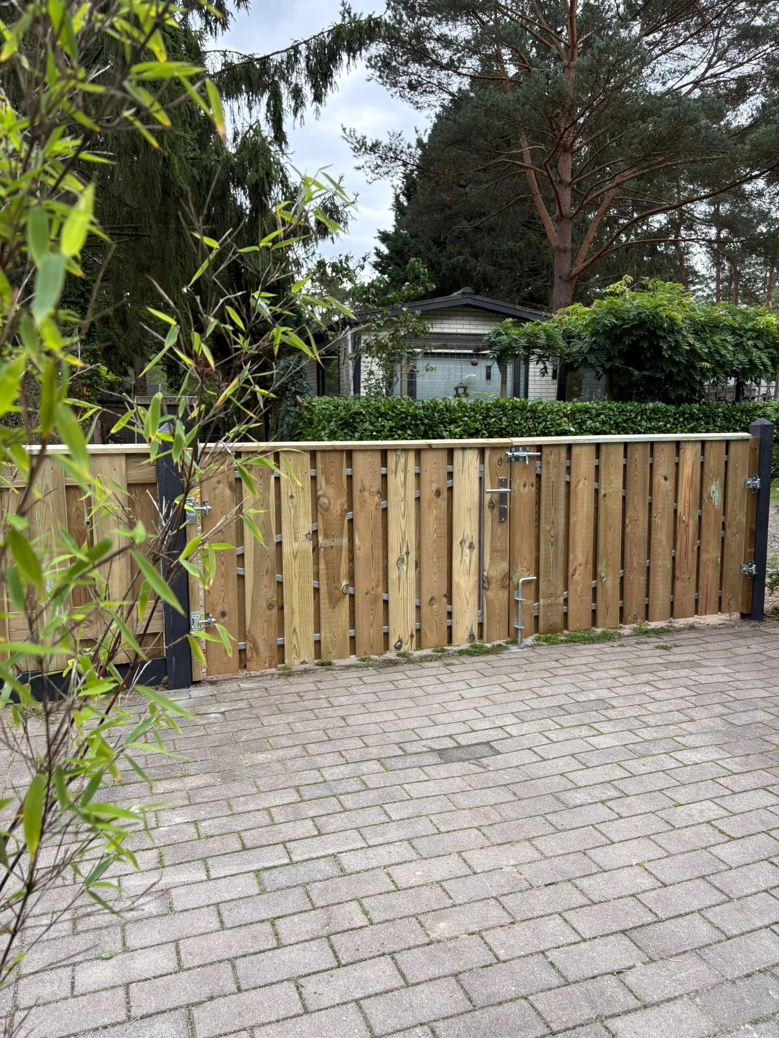 Houten poort met zwarte scharnieren en sloten in schutting geplaatst door Franke Tuinen