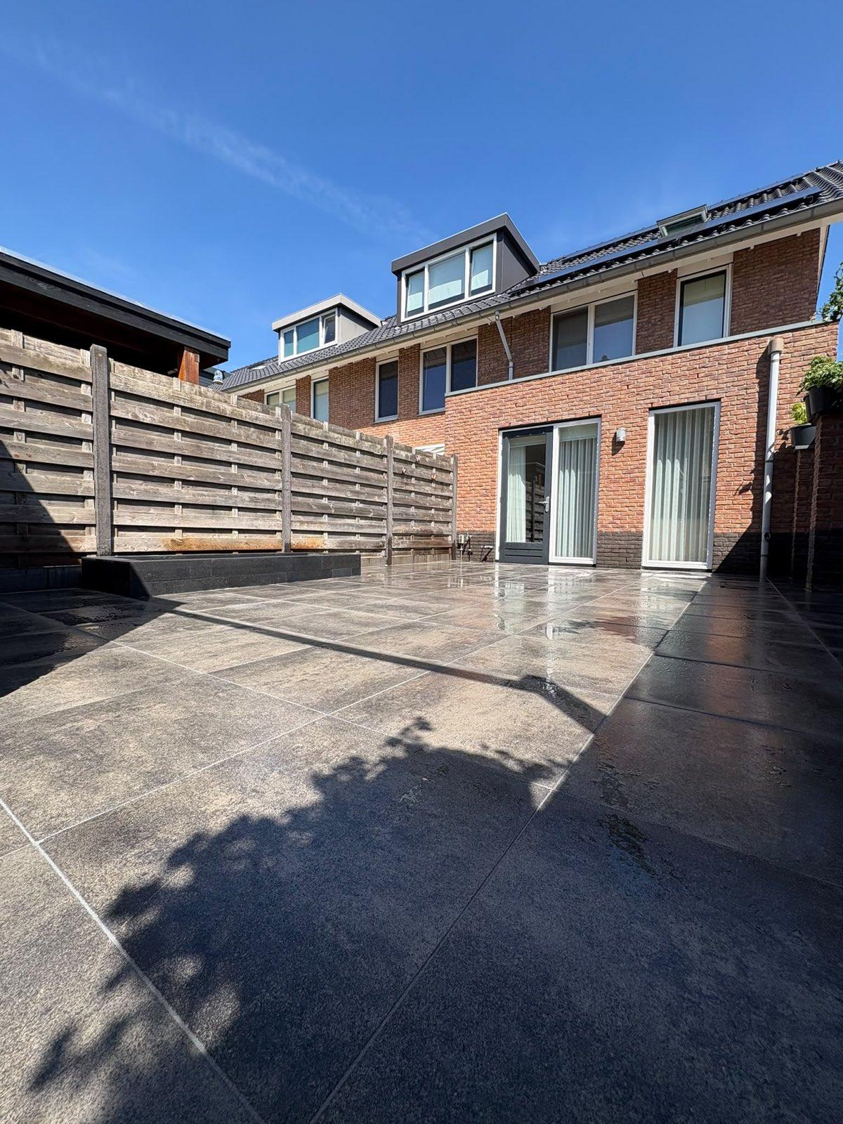 Ruim keramisch terras in de achtertuin aangelegd door Franke Tuinen